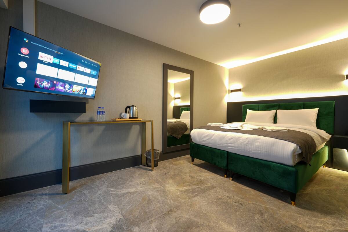 Una habitación de hotel con cama, televisor en la pared, mesita de noche y espejo.