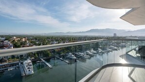Vista panorámica desde un balcón alto sobre un puerto deportivo con barcos, cielo despejado y montañas a lo lejos.