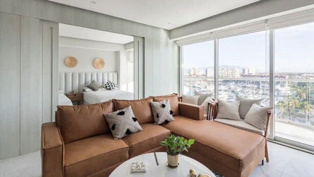 Una sala de estar moderna con un gran ventanal, un sofá de cuero marrón y vistas a la ciudad.