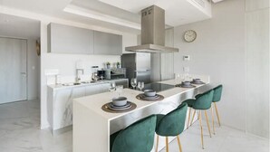 Una cocina moderna con una isla central, electrodomésticos de acero inoxidable y un comedor con sillas verdes.