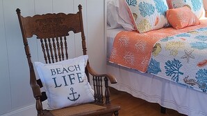 Un dormitorio con una mecedora de madera, una cama con ropa de cama colorida y un estante de pared con adornos.