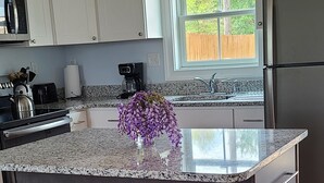 Una cocina moderna con encimera de granito, dos taburetes negros, una lámpara colgante y vistas al exterior a través de una ventana.