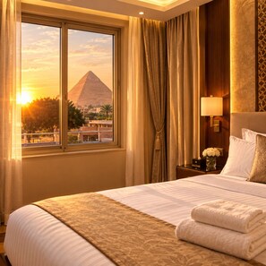 A hotel room with a bed, a nightstand, a lamp, and a view of a pyramid. - Sky pyramids  (Giza)