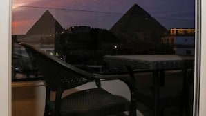 A balcony with two chairs and a table, overlooking pyramids at dusk. - Sky pyramids  (Giza)
