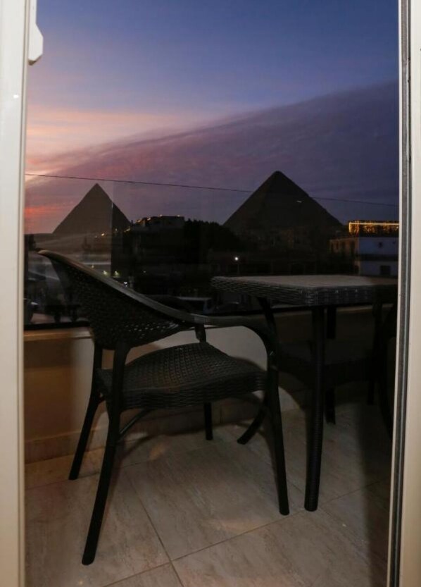 Un balcón con dos sillas y una mesa, con vistas a las pirámides al atardecer.