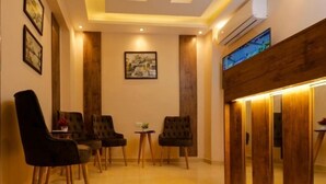 A hotel lobby with a wooden reception desk, several chairs, framed artwork on the walls, and a large window with a view. - Sky pyramids  (Giza)
