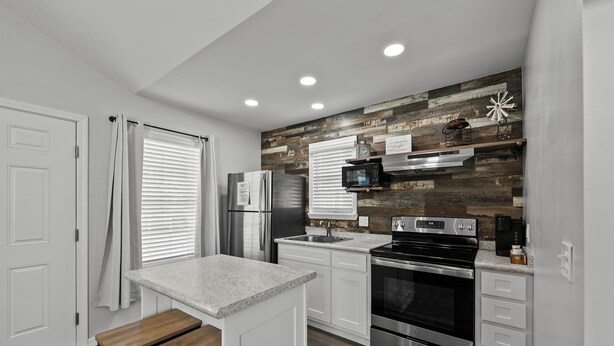 A modern kitchen with white cabinetry, stainless steel appliances, and a wooden accent wall. - "Live Oak" Cottage Reidsville Georgia (Reidsville)