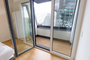 A modern room with a glass door leading to a balcony with a wooden floor and a city view.