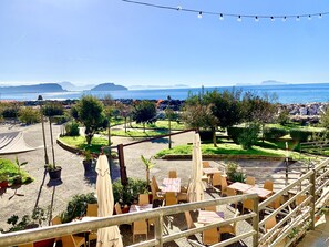 Una terraza con mobiliario exterior, vistas al mar y un paisaje montañoso en la distancia.