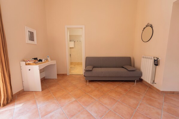 Una habitación con un sofá gris, un escritorio blanco y un radiador.
