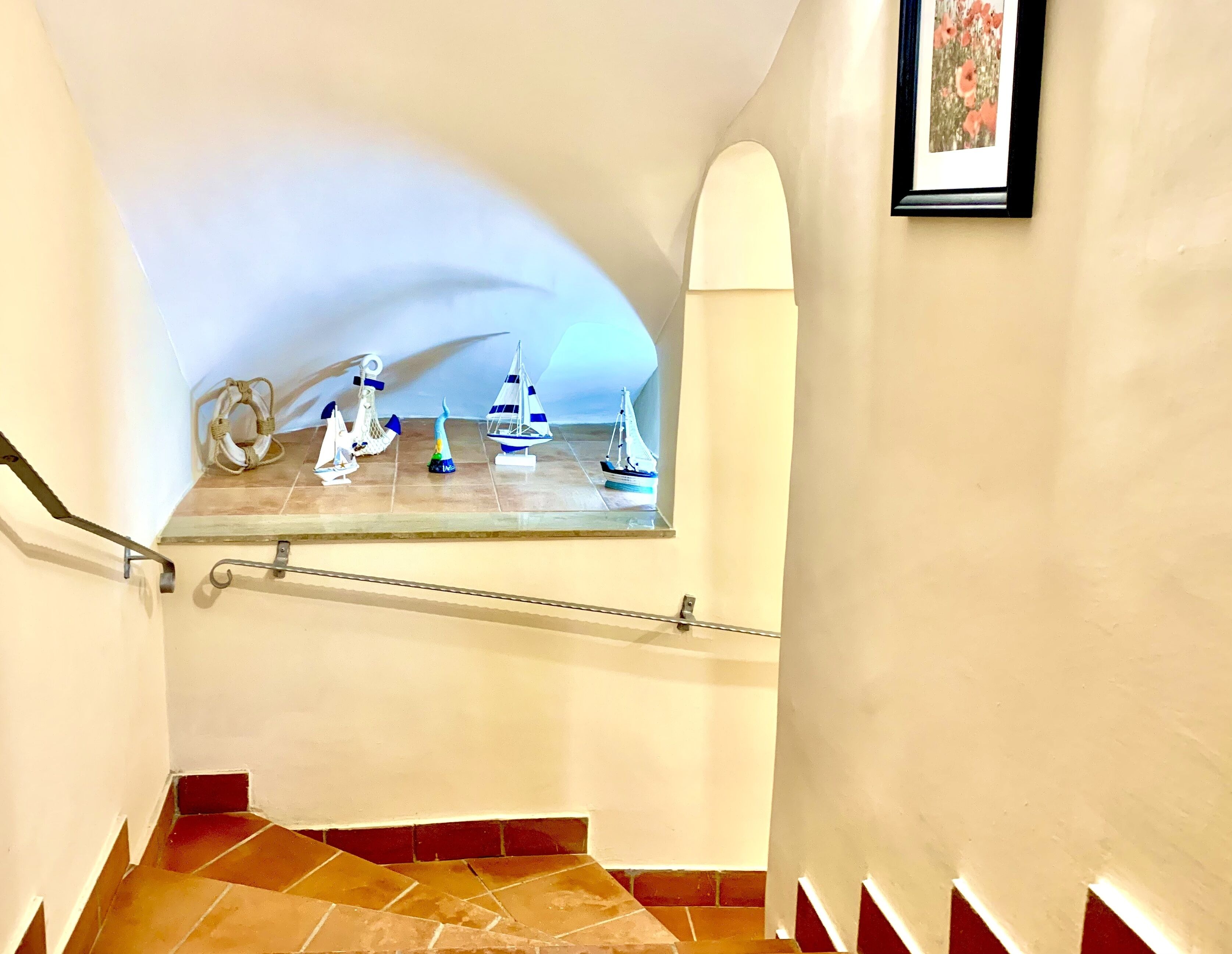Una scala con corrimano, un pavimento piastrellato e uno scaffale a parete con modellini di navi.
