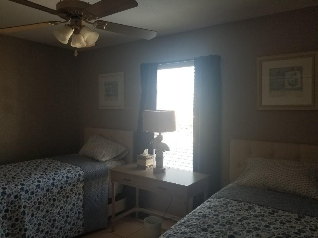 A bedroom with two beds, a desk, a ceiling fan, and a window with curtains.