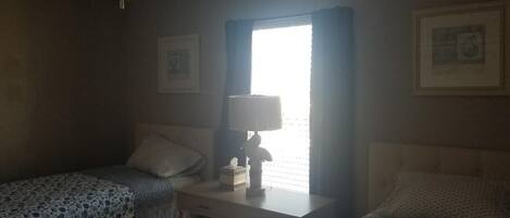 A bedroom with two beds, a desk, a ceiling fan, and a window with curtains.