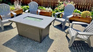A patio area with a rectangular table and four white chairs, surrounded by wooden planters with various plants. - Central Craftsman Apartment (Arcata)