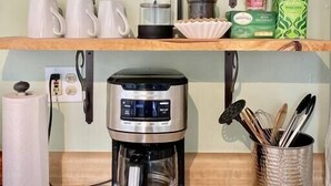 A kitchen with a coffee maker, a shelf with glassware, and a box of Stash coffee pods.