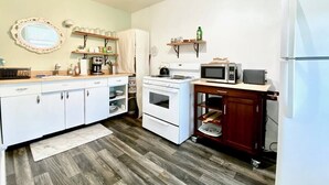 A compact kitchen with white cabinets, a stove, microwave, and a refrigerator.