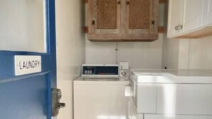 Une buanderie avec une porte bleue portant l’inscription « BUANDERIE », un lave-linge, un sèche-linge et des armoires en bois au-dessus.