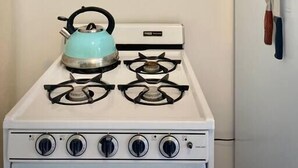Une cuisine équipée d’une cuisinière, d’une bouilloire, d’une étagère murale pour les épices, d’un élément décoratif mural et d’une horloge murale.