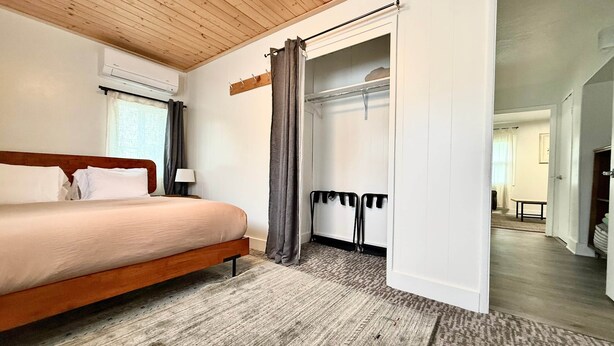 A bedroom with a wooden ceiling, a bed, a wardrobe, and a bathroom visible through an open door. - Downtown Arcata Stylish Apt (Arcata)