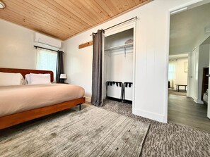 Une chambre avec un plafond en bois, un lit, une armoire et une salle de bain visible à travers une porte ouverte.