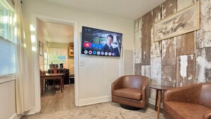 A living room with a flat-screen TV mounted on the wall, a brown leather armchair, a wooden coffee table, and a rustic wall panel. - Downtown Arcata Stylish Apt (Arcata)