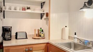 A compact kitchen with wooden cabinets, a sink, and a countertop. There are shelves above the counter holding cups and plates. - Downtown Arcata Stylish Apt (Arcata)
