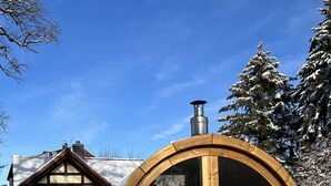 A wooden barrel structure with a chimney, set in a snowy landscape with a house in the background. - Upper mill (Sohland an der Spree)