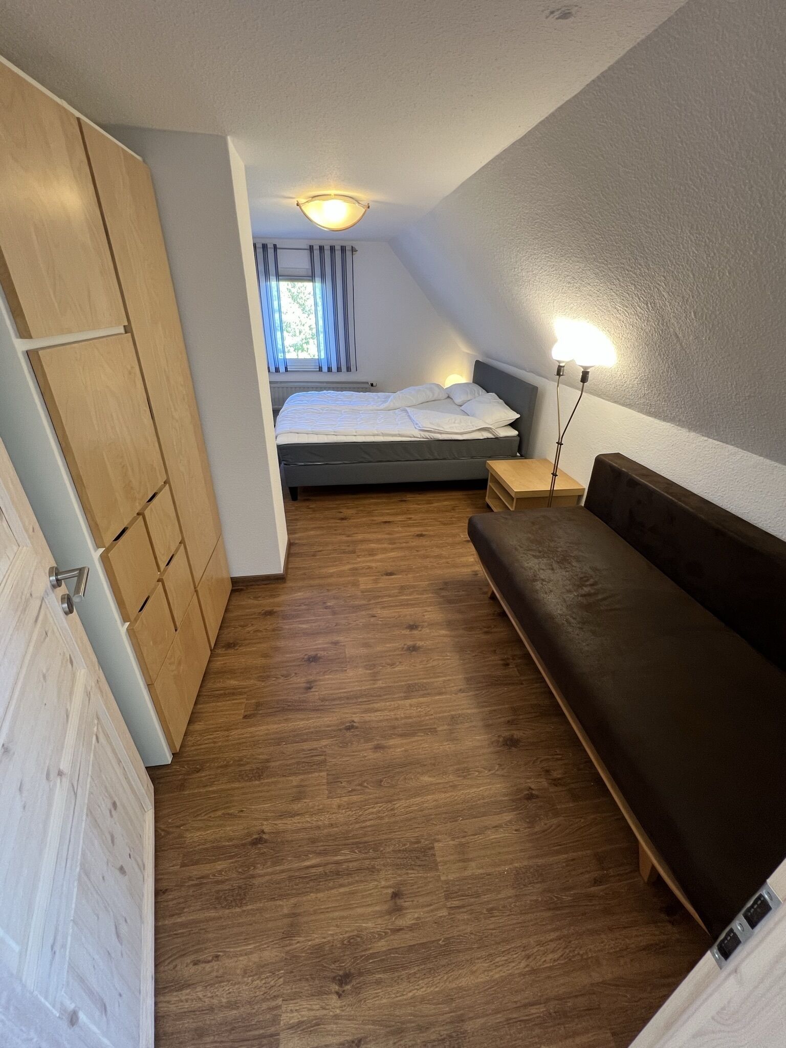 A bedroom with a bed, wooden wardrobe, and a bench.