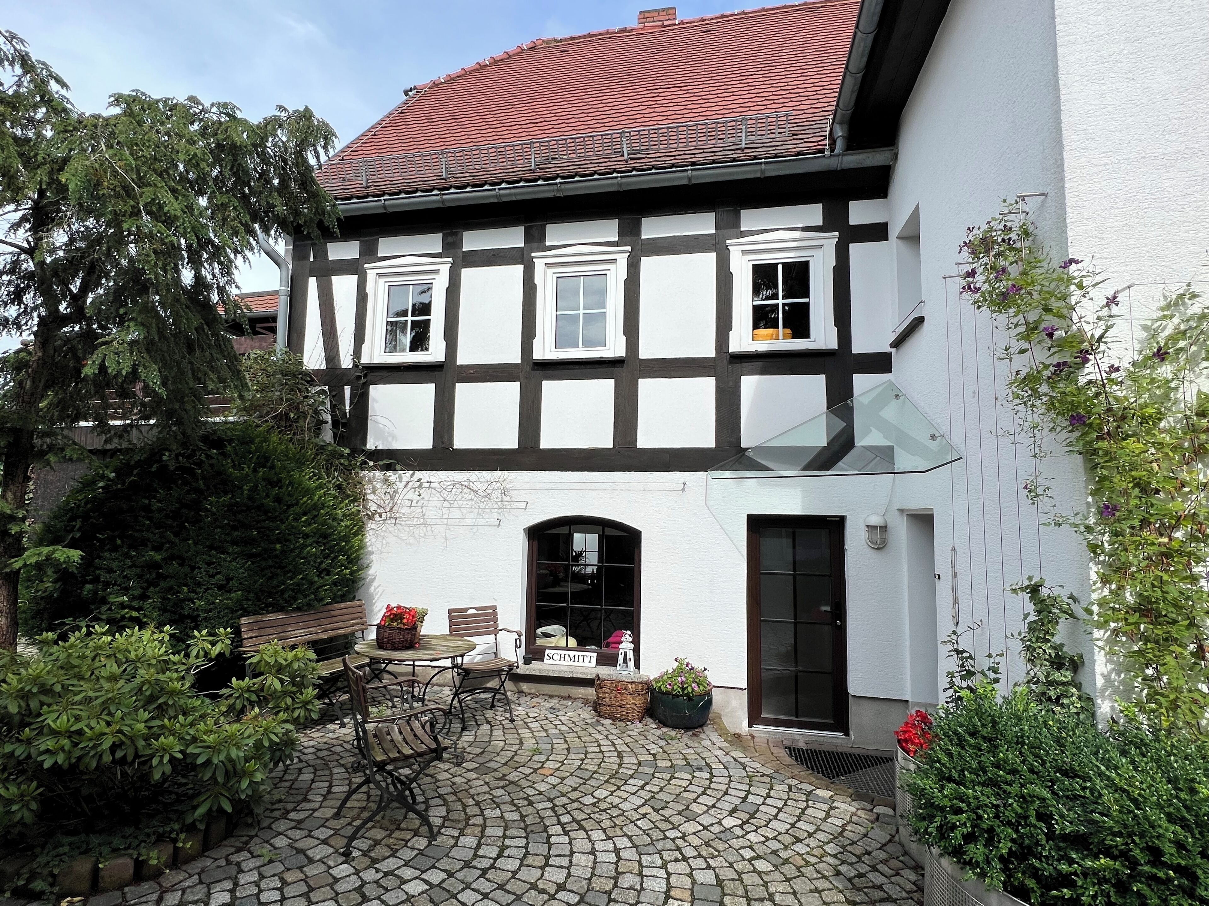 A traditional half-timbered house with a courtyard, a wooden bench, and potted plants.