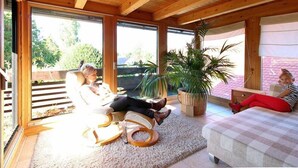 A spacious room with a wooden ceiling and large windows. There is a chair and a bed with a checkered bedspread. - Upper mill (Sohland an der Spree)