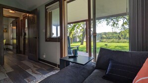 A modern living room with a sofa, a small table, and a view of a lush garden through large sliding glass doors. - Dogs Stay Free!  Lakefront Bungalow with Dock (Juneau)