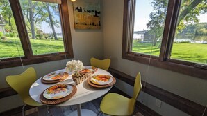 A dining area with a round table, yellow chairs, and a view of a lake through large windows. - Dogs Stay Free!  Lakefront Bungalow with Dock (Juneau)