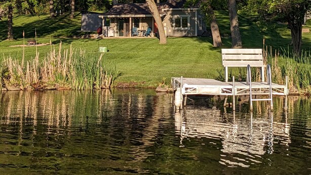 A lakeside property with a dock, a bench, and a small building with a porch. - Dogs Stay Free!  Lakefront Bungalow with Dock (Juneau)