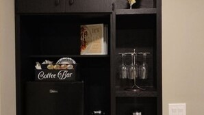 A black wall with a shelf containing a coffee bar, a decorative leaf, and a wine glass holder.