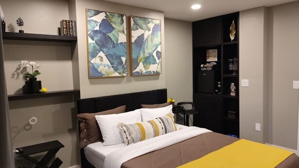 A bedroom with a bed, a nightstand, a shelf with decorative items, and two abstract paintings on the wall.
