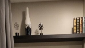 A room with a black shelf holding a potted plant, a small vase, and a fruit bowl.