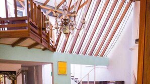 A dining area with a wooden table and chairs, a chandelier, and a staircase leading to an upper level. - Gaudys Hotel (San José)