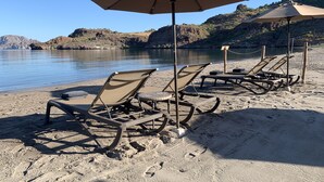 A beach with sun loungers and umbrellas, a calm lake, and rocky hills in the background. - Luxury Suite, The Islands of Loreto - stunning natural beauty in Mexico (Loreto)