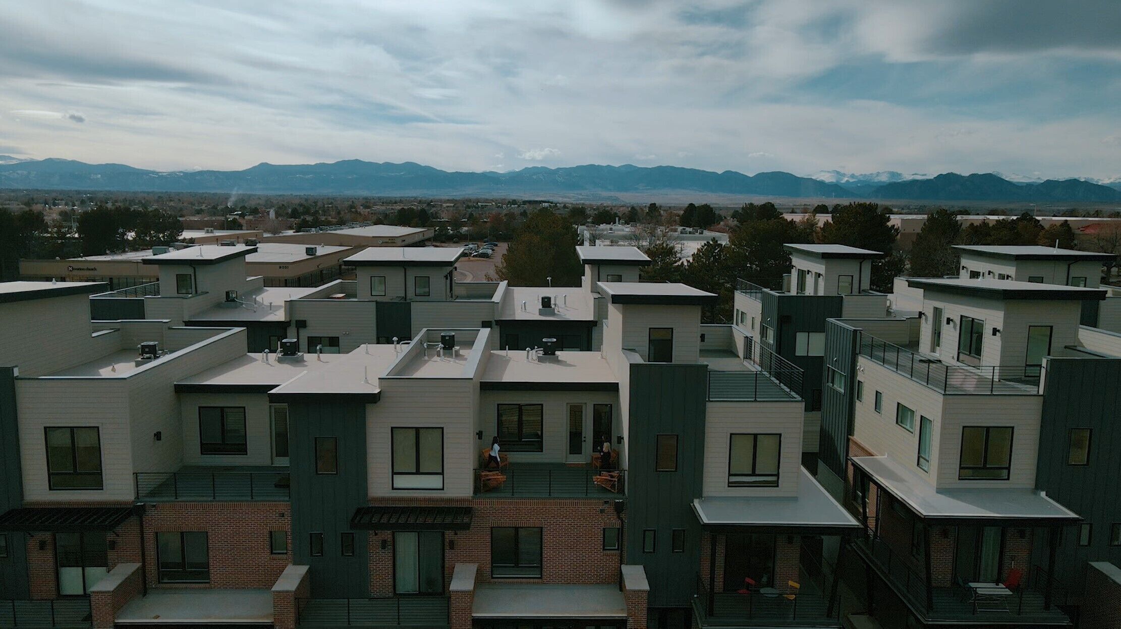A modern residential complex with multiple buildings, flat roofs, and a mountainous backdrop.