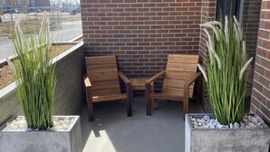 Eine Terrasse mit zwei Holzstühlen und zwei quadratischen Pflanzgefäßen mit hohem Gras.