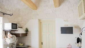 A kitchen with a stone wall, wooden beams, a microwave, a sink, and a door with a light switch above it. - COMPLEX OF TRULLI WITH POOL IN THE COUNTRYSIDE. GREAT POSITION: TRULLETTO  (MARTINA FRANCA)