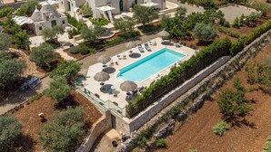 An aerial view of a villa with a swimming pool, stone architecture, and surrounding greenery. - COMPLEX OF TRULLI WITH POOL IN THE COUNTRYSIDE. GREAT POSITION: TRULLETTO  (MARTINA FRANCA)