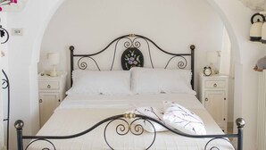 A bedroom with a bed under an arched ceiling, a nightstand with a lamp, and a wall clock. - COMPLEX OF TRULLI WITH POOL IN THE COUNTRYSIDE. GREAT POSITION: TRULLETTO  (MARTINA FRANCA)
