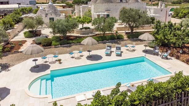 A swimming pool with lounge chairs and umbrellas, surrounded by stone buildings and greenery. - COMPLEX OF TRULLI WITH POOL IN THE COUNTRYSIDE. GREAT POSITION: TRULLETTO  (MARTINA FRANCA)