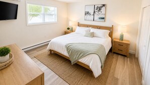 A bedroom with a bed, bedside tables, a TV, a window, and artwork on the wall.