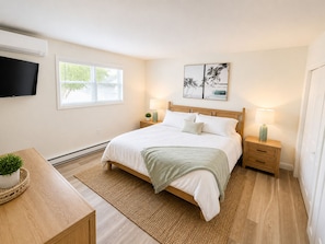 A bedroom with a bed, bedside tables, a TV, a window, and artwork on the wall.