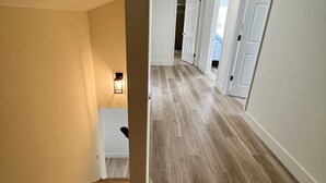 A hallway with wooden flooring, white walls, and a staircase leading to another room.