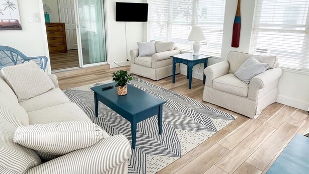 A living room with a sofa, two armchairs, a coffee table, a TV, and a ceiling fan.