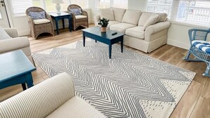 A living room with a beige sofa, two wicker chairs, a blue coffee table, and a patterned rug.