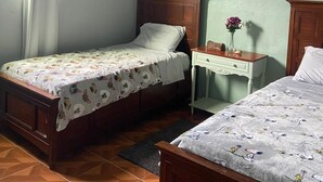 Une chambre avec deux lits, un ventilateur de plafond, une table de chevet et une fenêtre avec des rideaux.